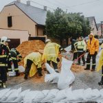 Equipe de emergência coloca sacos de areia em uma rua molhada para conter possíveis alagamentos.